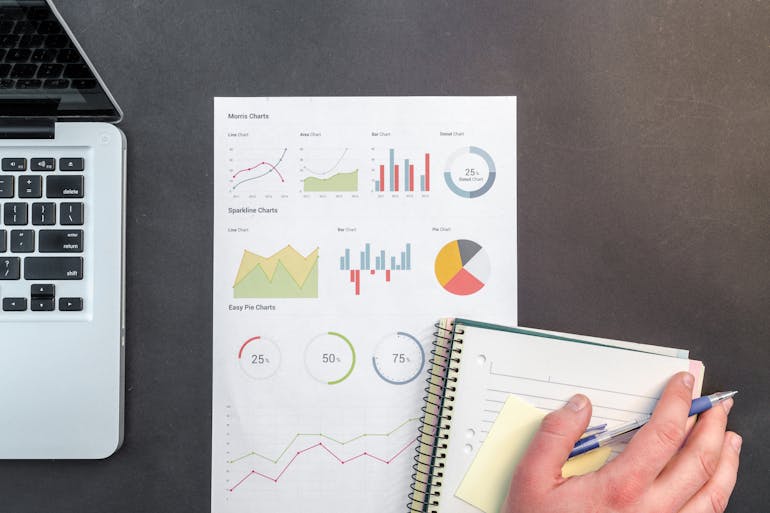 A hand on a notebook next to a piece of paper with charts on it